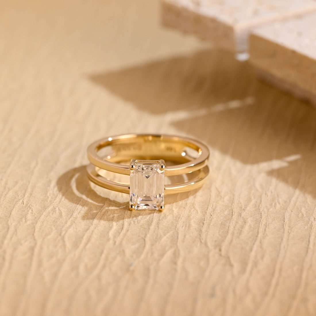 Emerald cut moissanite solitaire engagement ring on a double band split shank of two parallel polished yellow gold bands