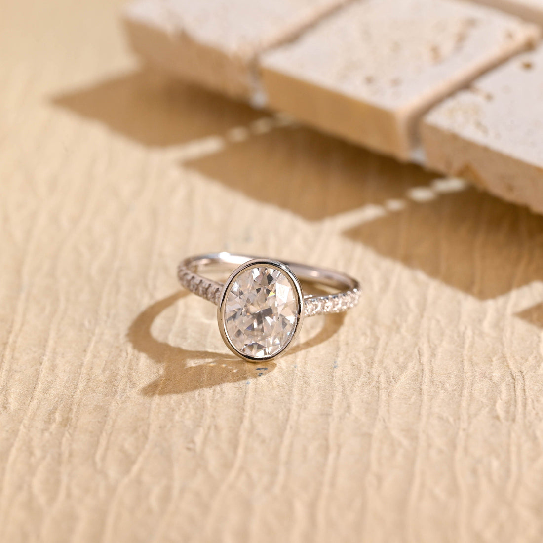 Bezel set oval moissanite engagement ring on a slim white gold band set with small round stones