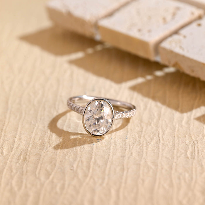 Bezel set oval moissanite engagement ring on a slim white gold band set with small round stones