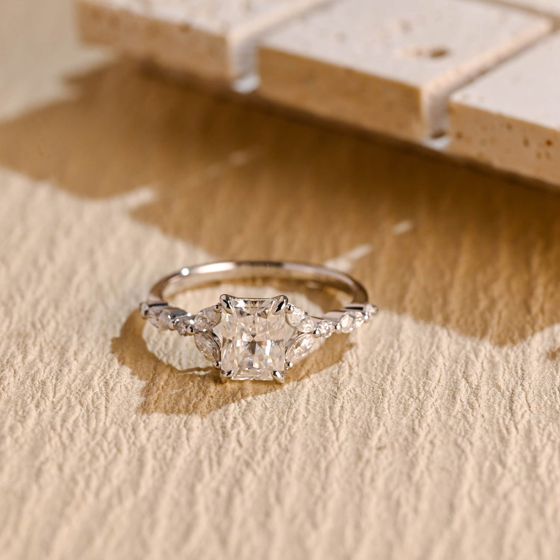 Radiant cut moissanite engagement ring with pairs of marquise stones at each side and a band set with alternating round and marquise stones in white gold