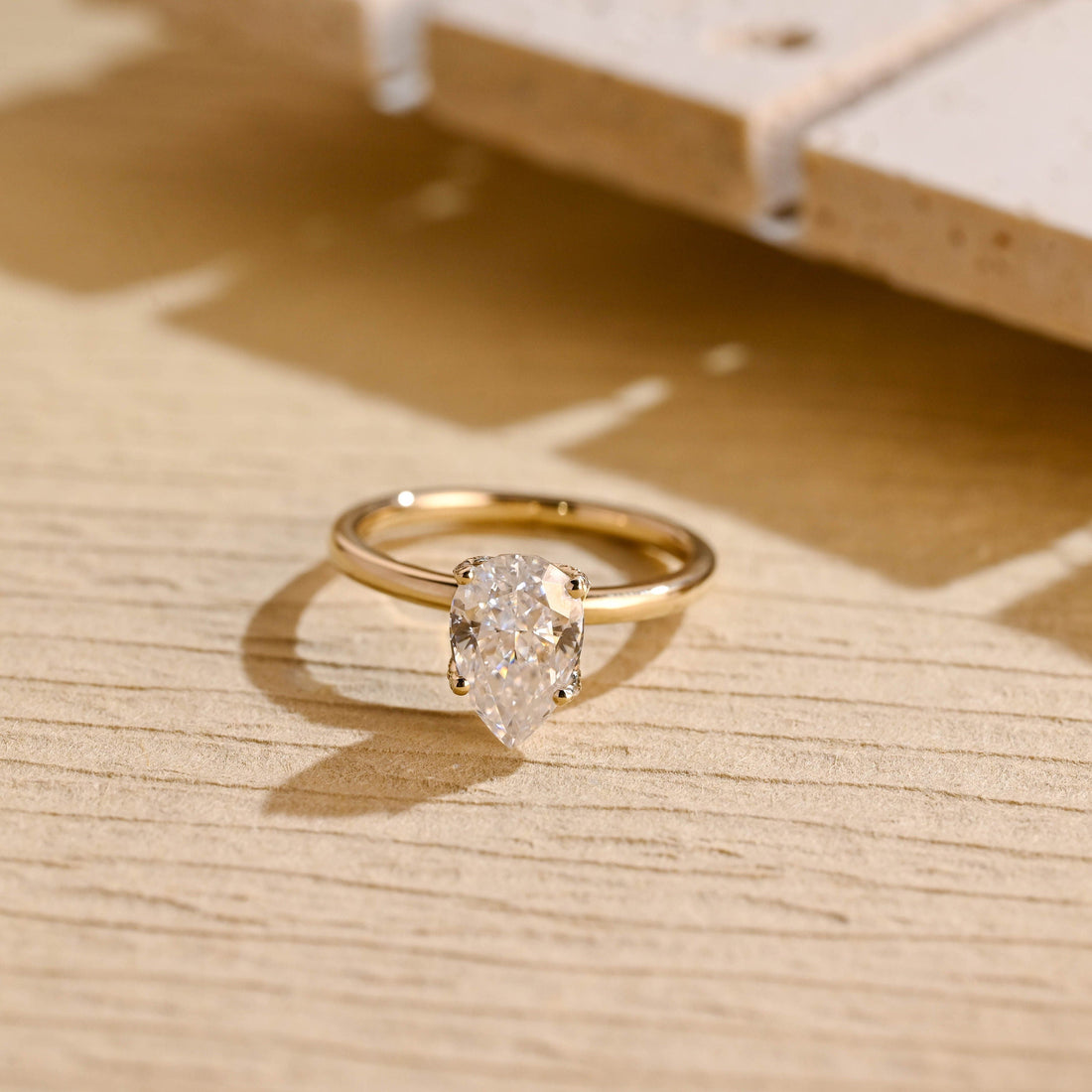 Pear cut moissanite solitaire engagement ring in a tulip style four claw setting with tiny hidden accent stones on a plain yellow gold band