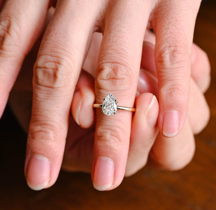Pear shaped moissanite engagement ring in four tulip claws with tiny stones beneath the stone on a slim polished yellow gold band, view 2