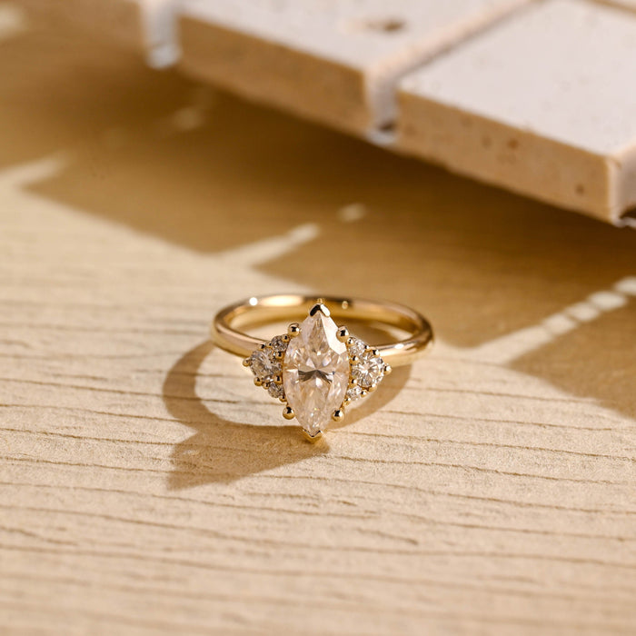 Marquise cut moissanite cluster engagement ring with a trio of round stones on each side on a plain yellow gold band