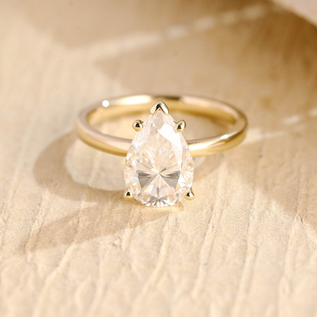 Large pear moissanite solitaire engagement ring with a V tip claw at the point and four ball claws on a polished yellow gold band