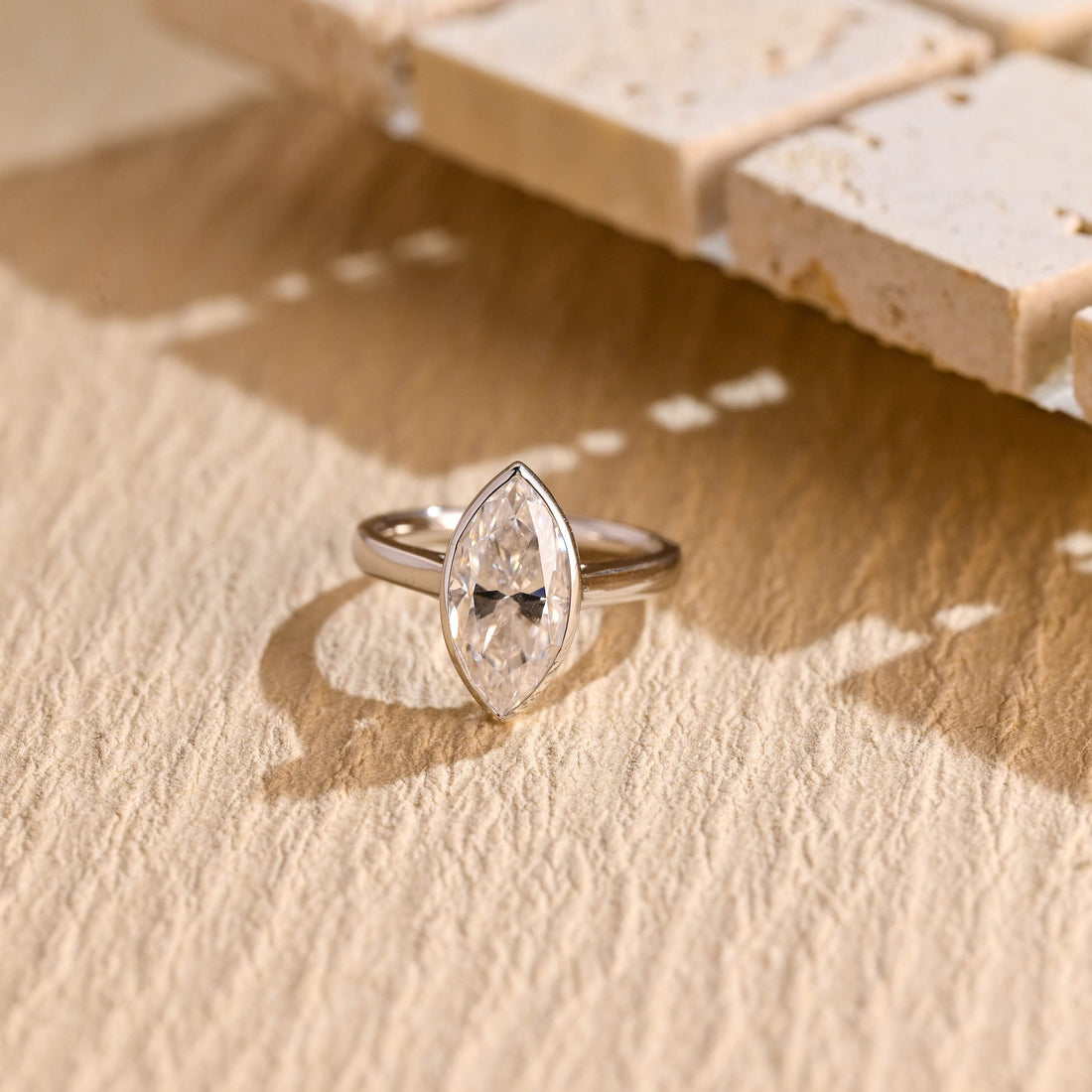 Bezel set marquise cut moissanite solitaire engagement ring on a wide tapered polished white gold band