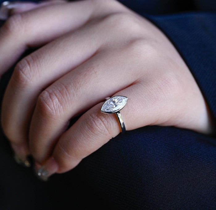 Bezel set marquise cut moissanite solitaire engagement ring on a wide tapered polished white gold band, view 2