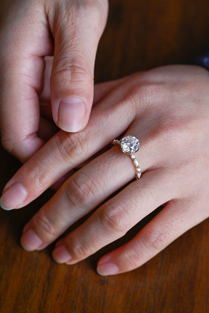 Round moissanite solitaire engagement ring in six claws with a slim yellow gold band set with alternating marquise and small round stones, view 2