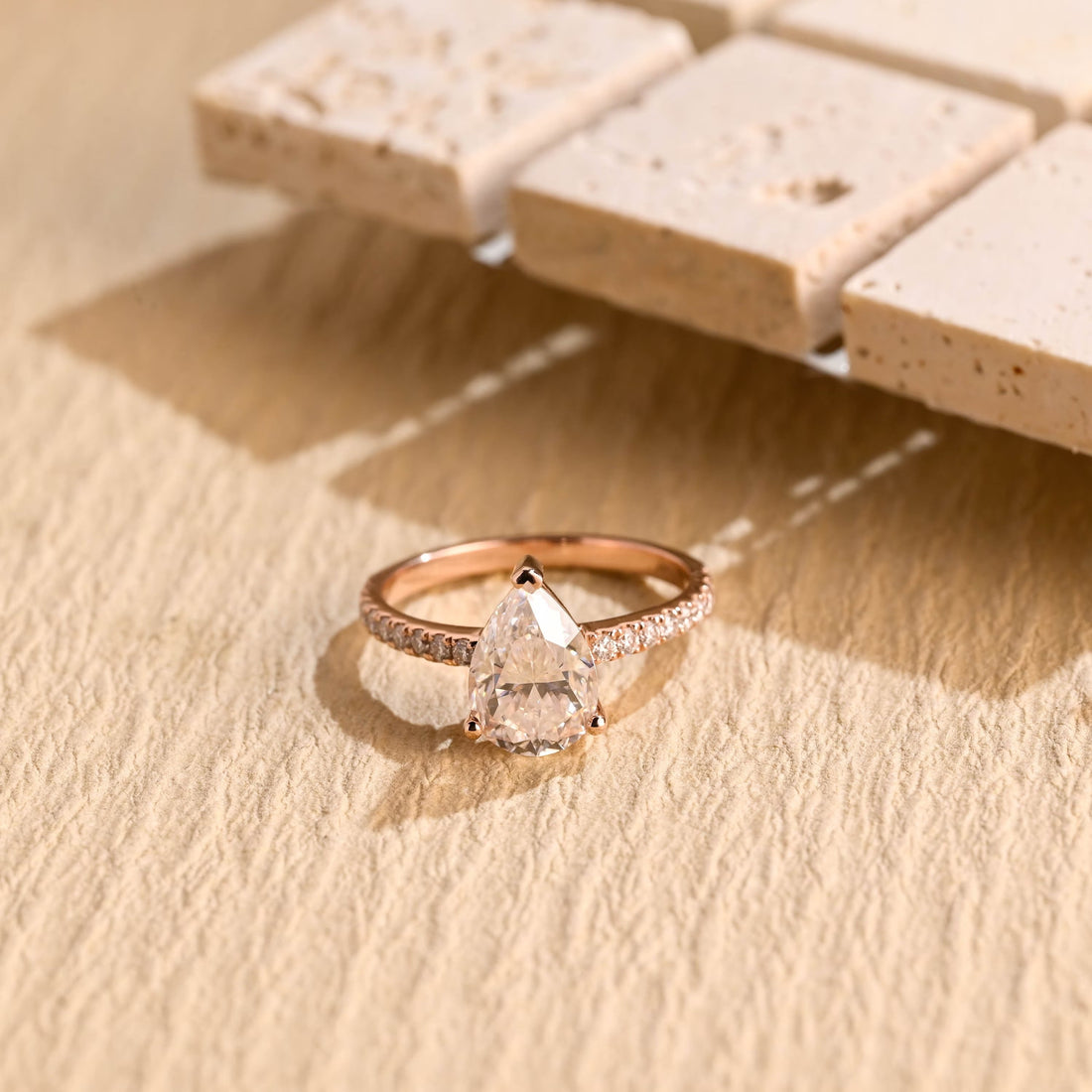 Pear cut moissanite engagement ring in three claws with a heart shaped tip claw on a slim rose gold band set with graduated pave stones