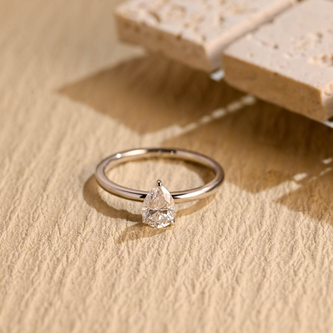 Pear cut moissanite solitaire engagement ring held by three fine claws on a thin plain round white gold band