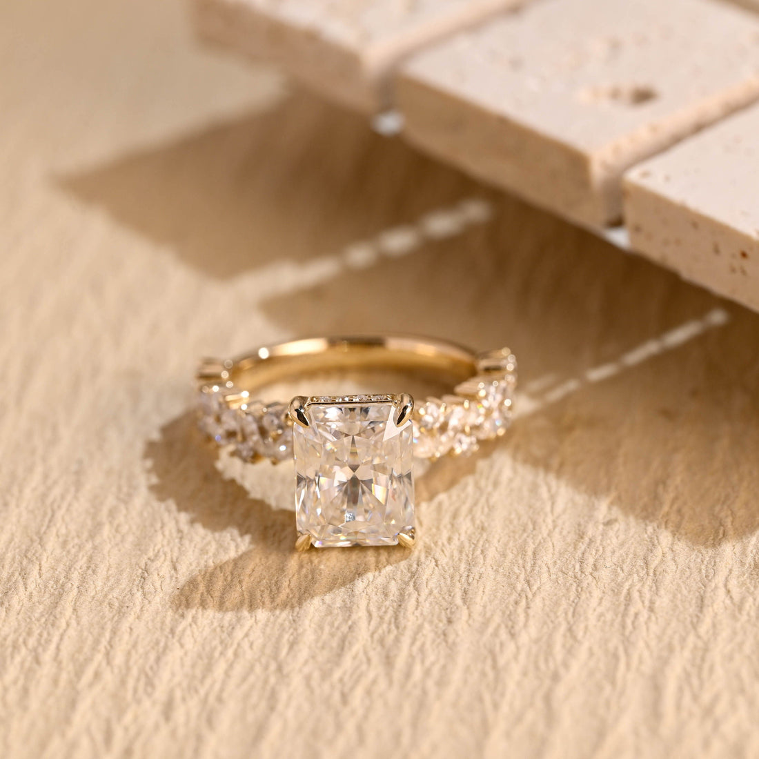Radiant cut moissanite hidden halo engagement ring in four claws with a band of scattered marquise and round stones in yellow gold