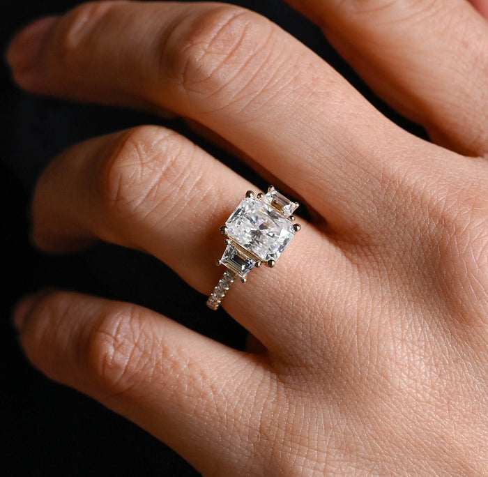 Radiant cut moissanite three stone engagement ring with tapered baguette side stones in claws and a pave set yellow gold band, view 2