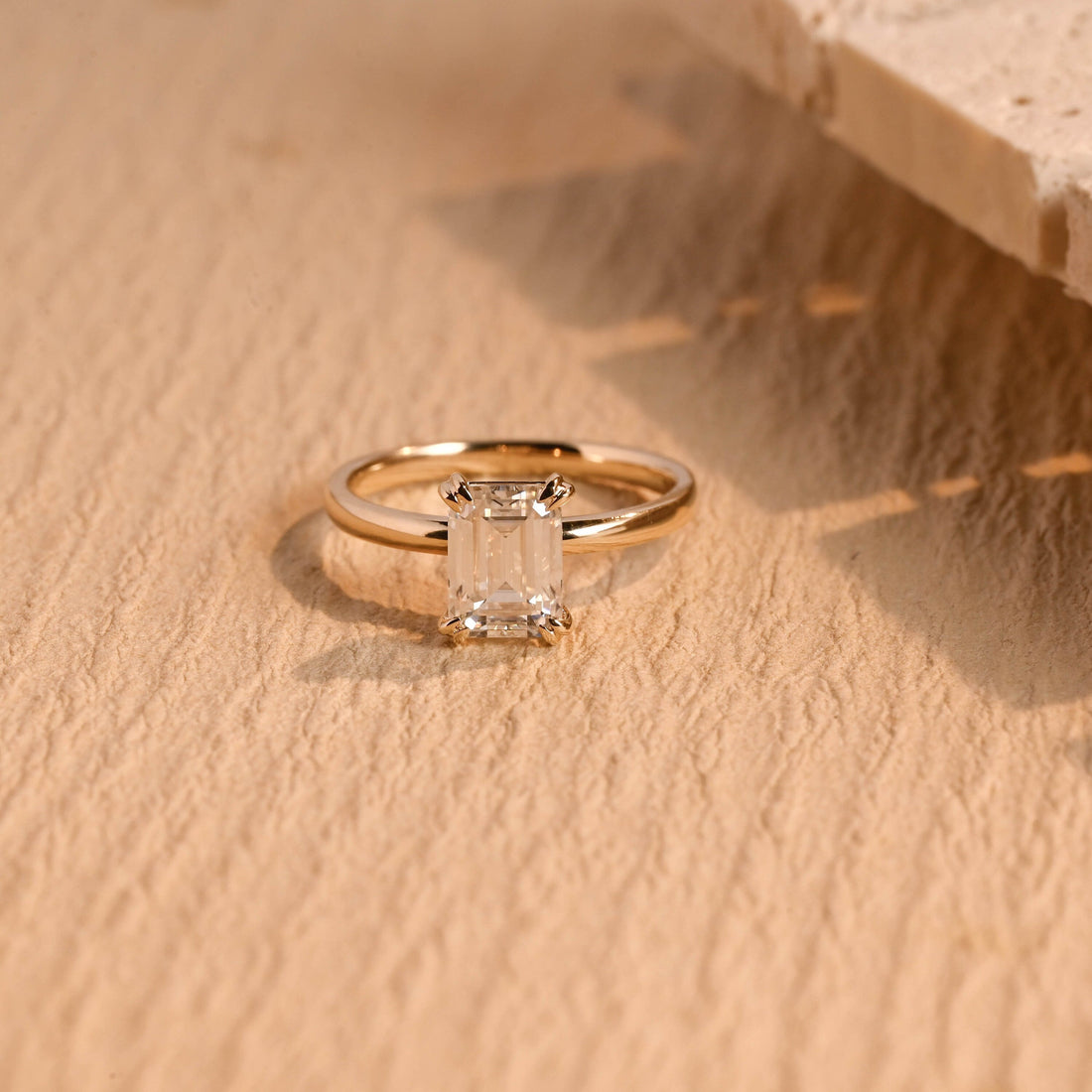 Classic emerald cut moissanite solitaire engagement ring held by twin round tipped claws at each corner on a smooth rounded yellow gold band