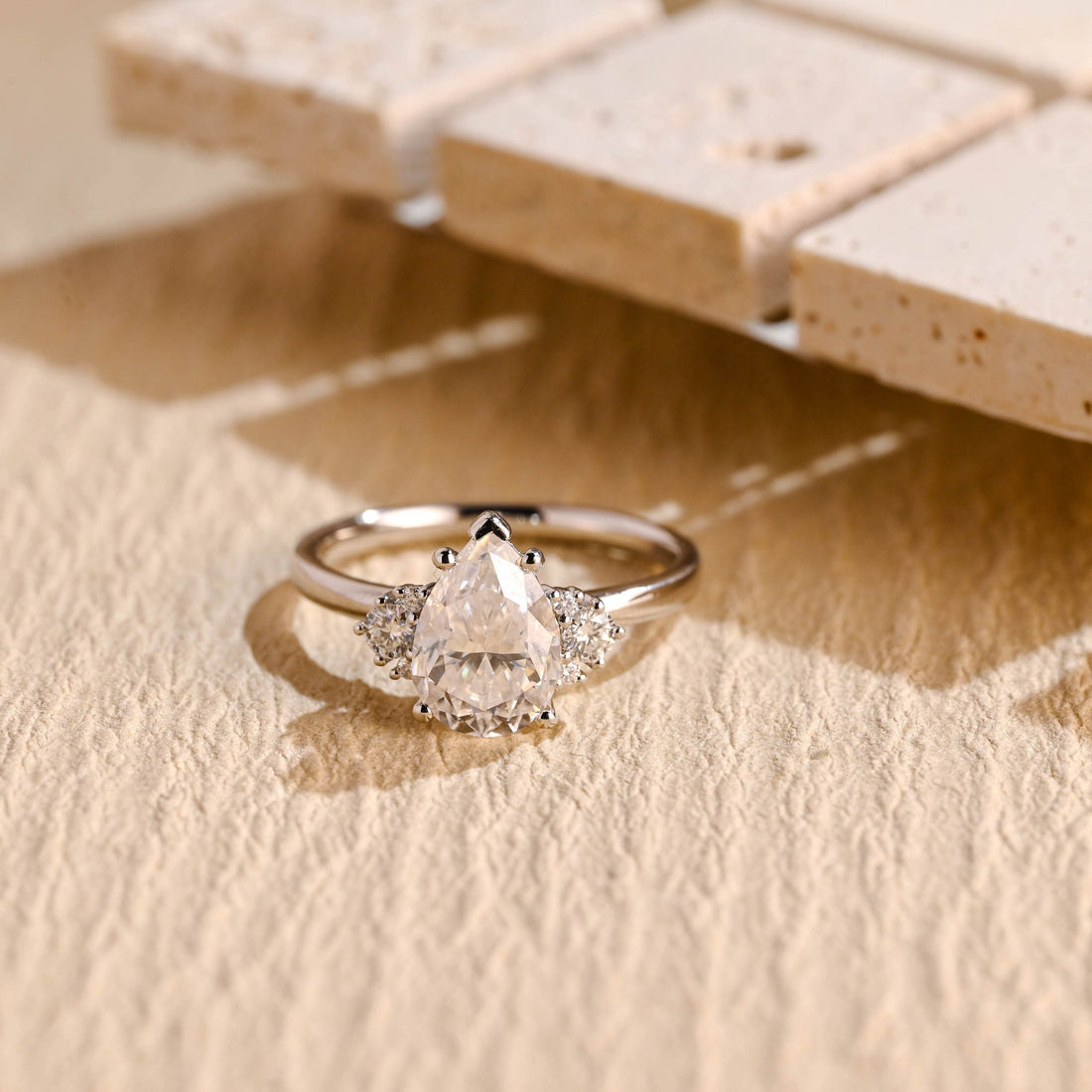 Pear cut moissanite engagement ring with a cluster of three small round stones on each side of the pear on a smooth white gold band
