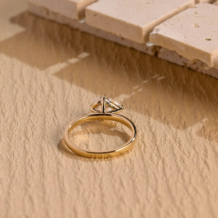 Tilted east west pear moissanite solitaire engagement ring in four slim claws on a smooth polished yellow gold band, view 2