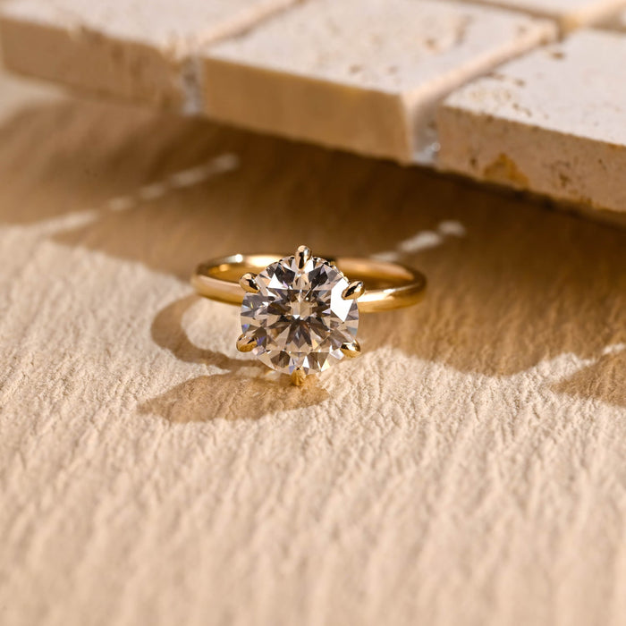 Round moissanite hidden halo engagement ring in six slender claws on a slim rounded yellow gold band