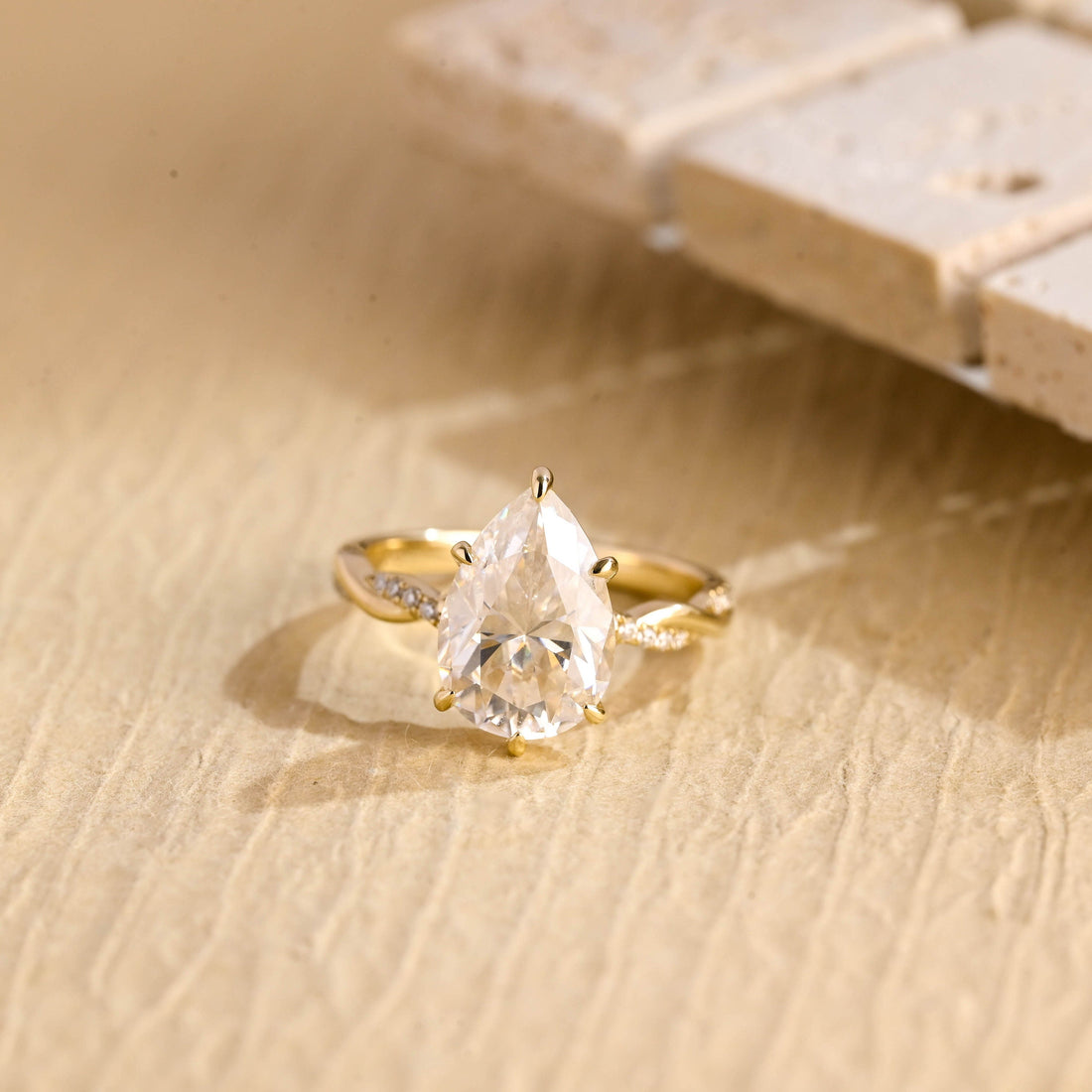 Pear cut moissanite engagement ring in six claws with a hidden halo and a twisted infinity pave set yellow gold band