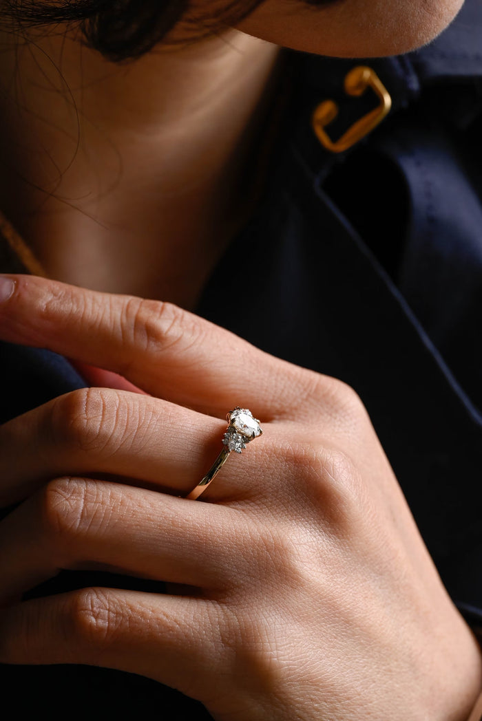 Oval moissanite cluster engagement ring with a pear and three small round stones on each side of the oval on a slim plain yellow gold band, view 2