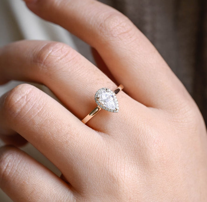 Pear shaped moissanite halo engagement ring with a teardrop halo of tiny round stones on a slim tapered polished yellow gold band, view 2