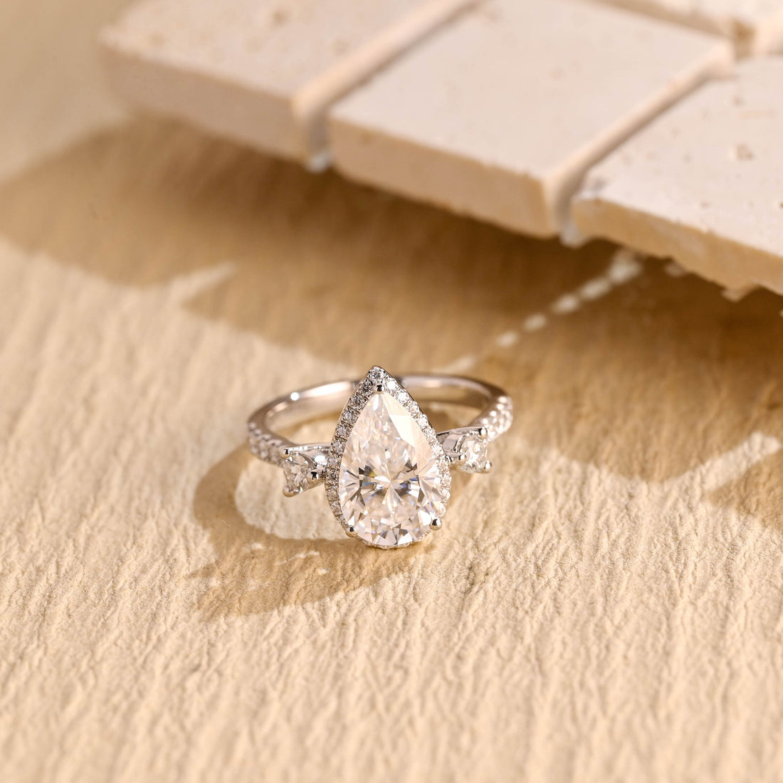 Pear cut moissanite halo engagement ring with a round stone on each side and a pave set white gold band