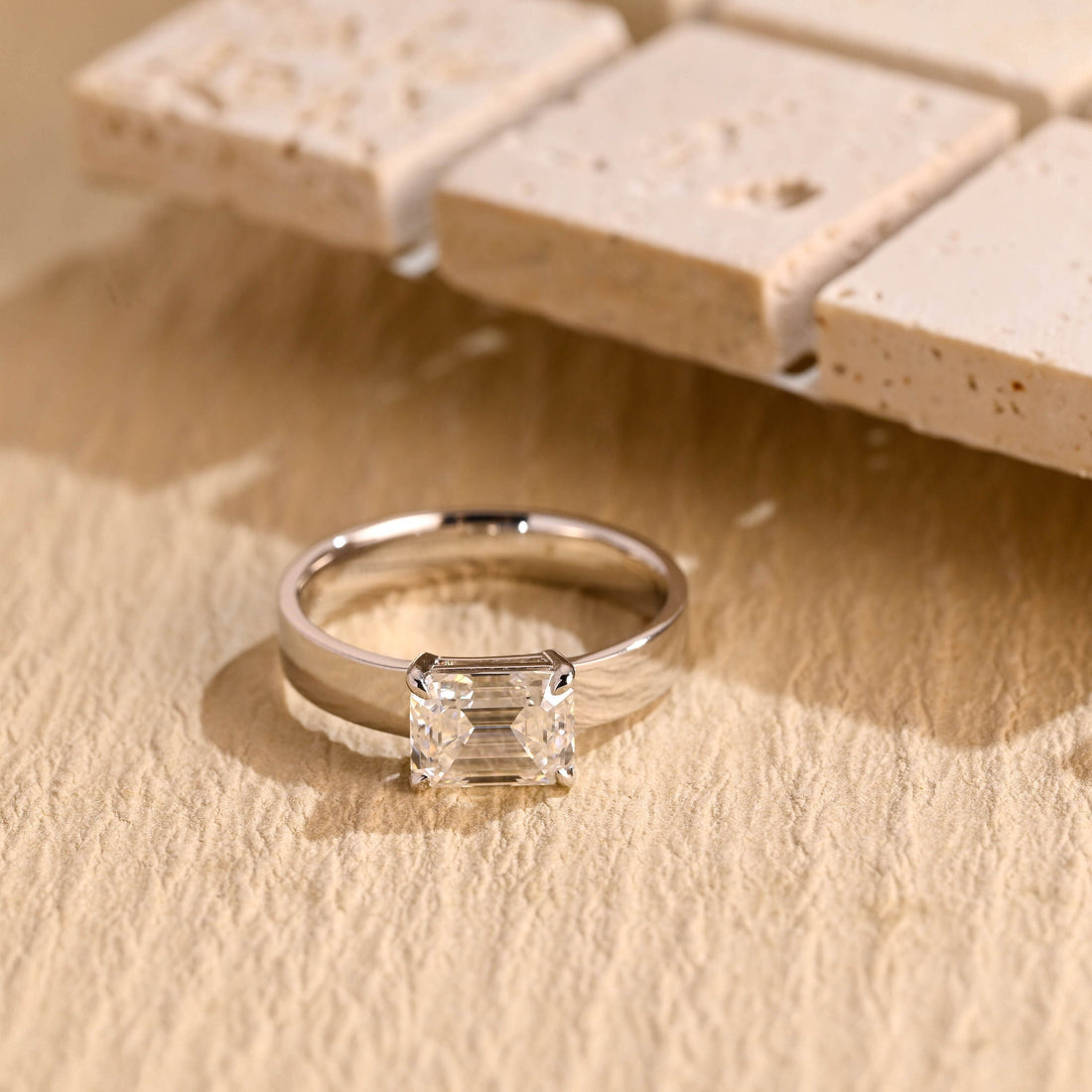 East west emerald cut moissanite solitaire engagement ring on a wide flat polished white gold band