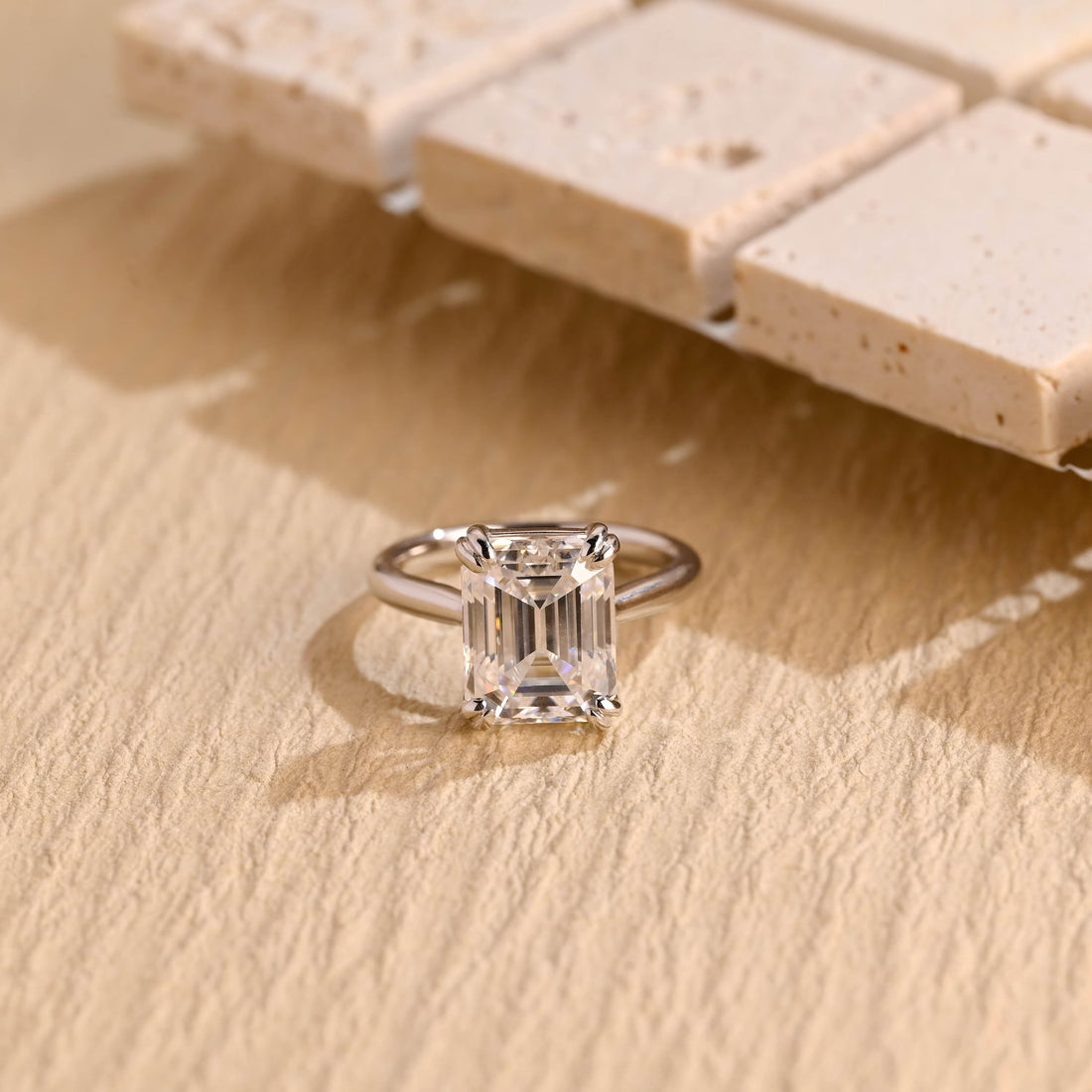 Statement emerald cut moissanite solitaire engagement ring held by double claws at each corner on a slim polished white gold band
