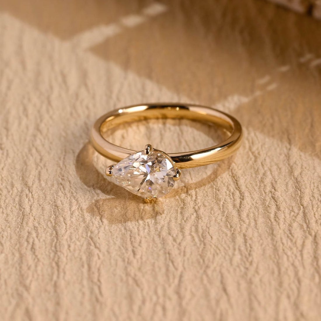 Tilted east west pear moissanite solitaire engagement ring in four slim claws on a smooth polished yellow gold band