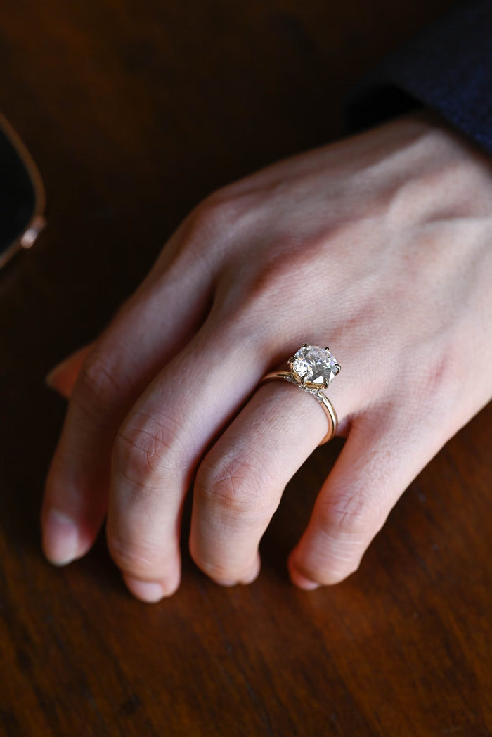 Round moissanite hidden halo engagement ring in six slender claws on a slim rounded yellow gold band, view 2