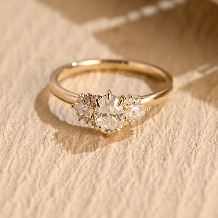 Oval moissanite cluster engagement ring with a pear and three small round stones on each side of the oval on a slim plain yellow gold band