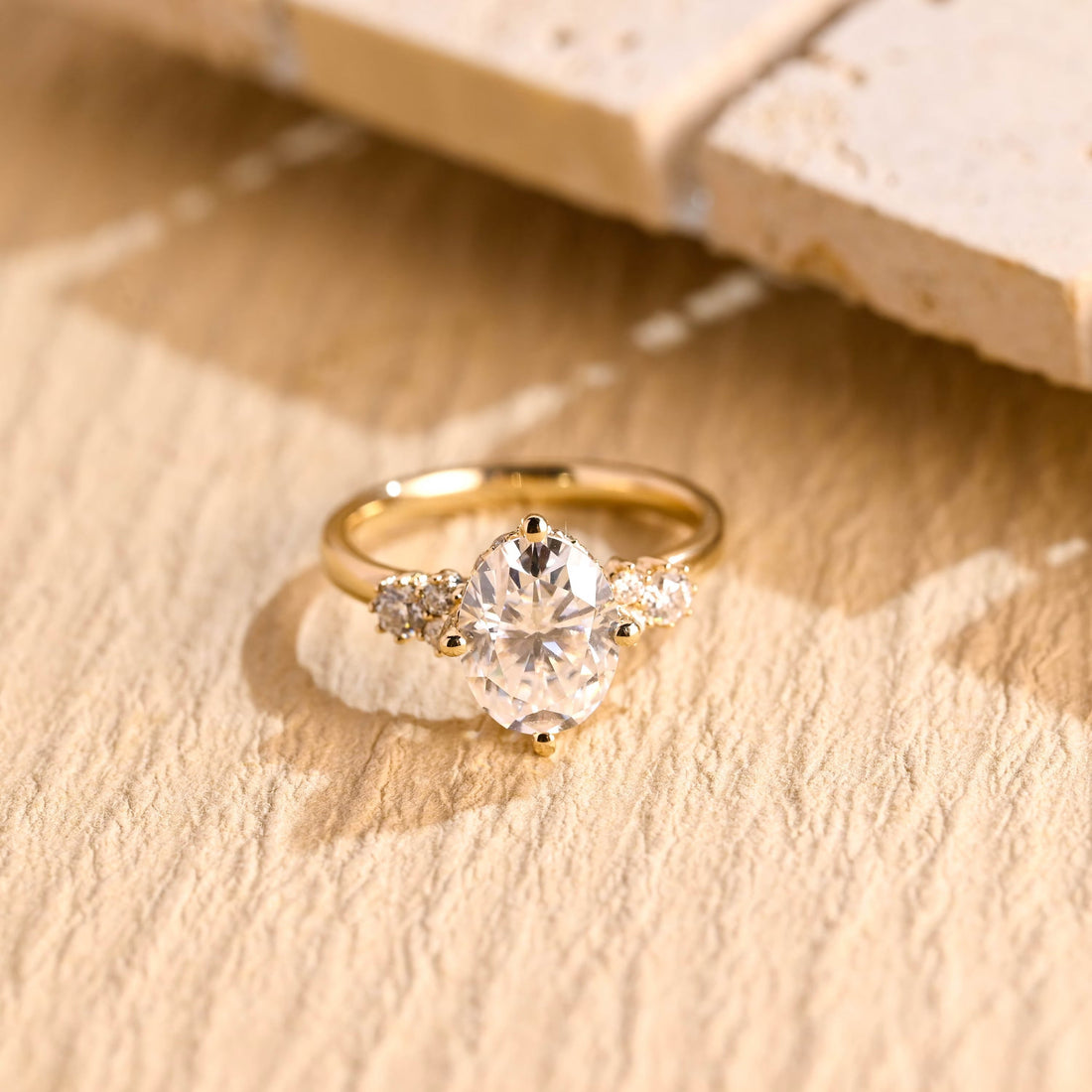 Oval moissanite engagement ring held by four compass point claws with a cluster of small round stones on each side on a slim plain yellow gold band