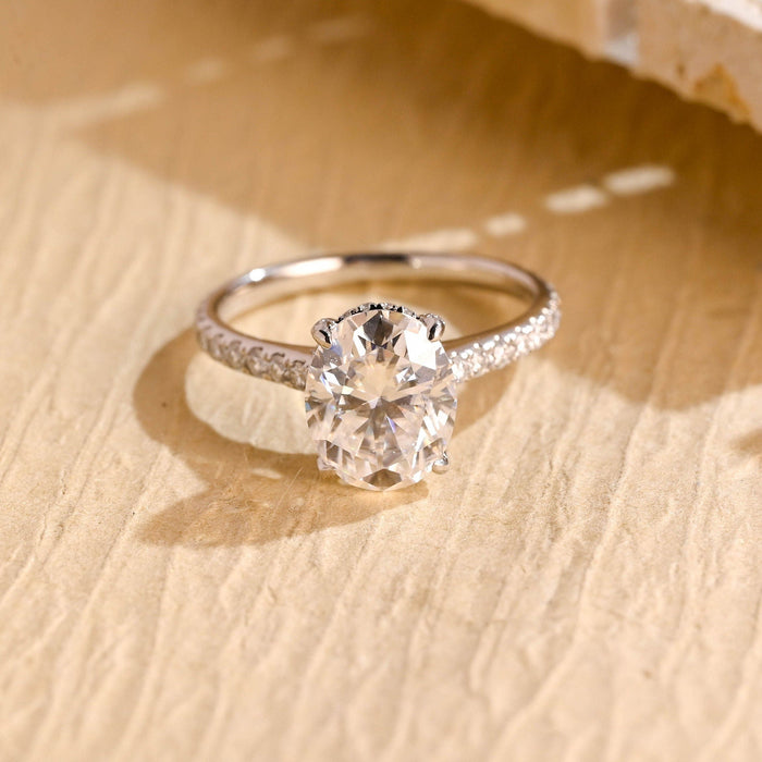Oval moissanite hidden halo solitaire engagement ring with four claws and a slender white gold band set with fine round stones