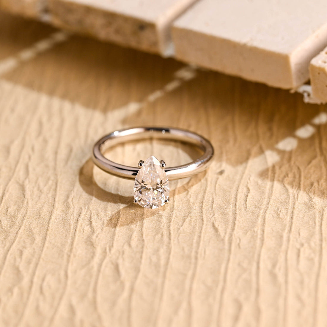 Petite pear moissanite solitaire engagement ring set point up in four claws on a smooth rounded white gold band