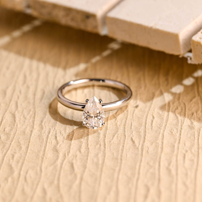 Petite pear moissanite solitaire engagement ring set point up in four claws on a smooth rounded white gold band