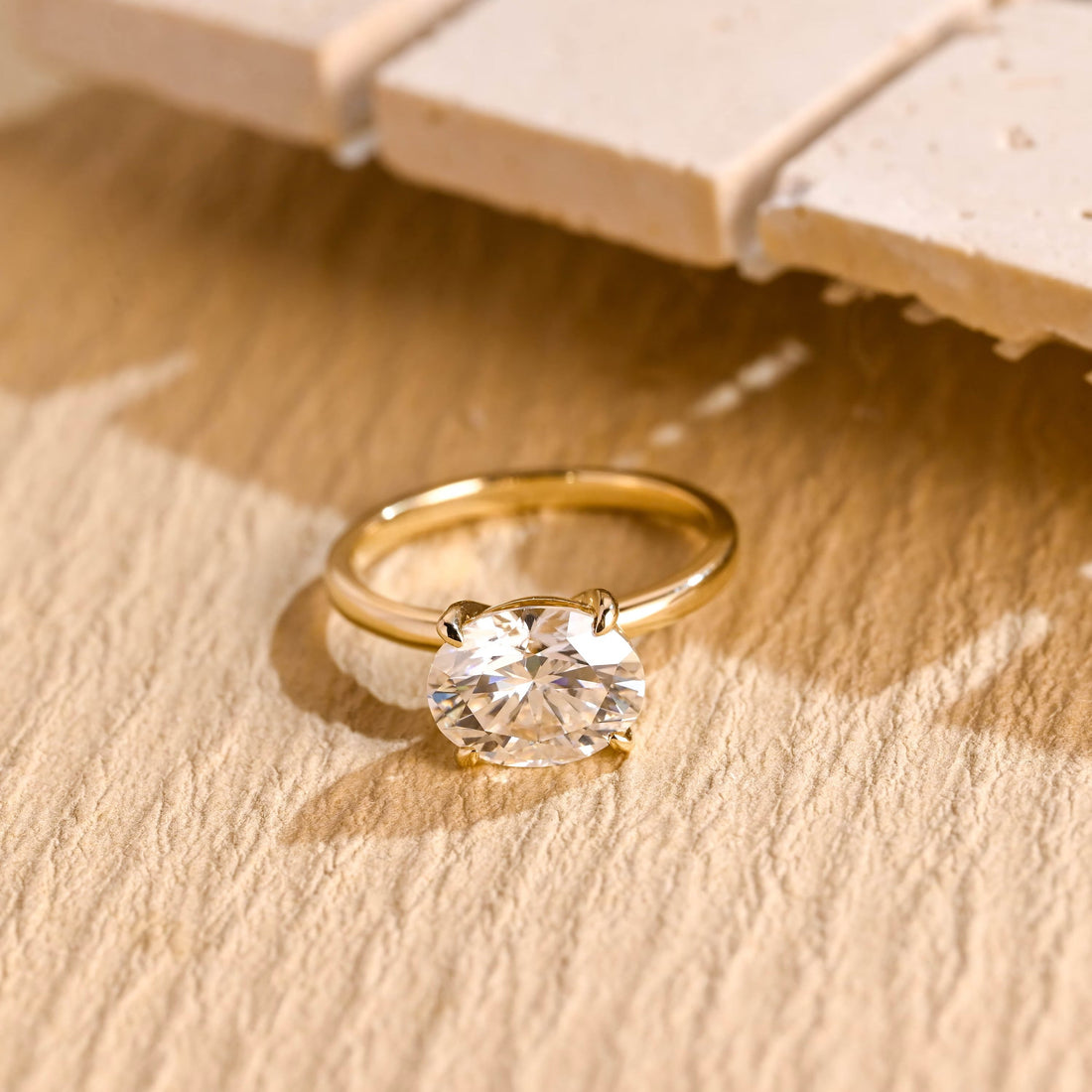 East west oval moissanite solitaire engagement ring set sideways in four slim claws on a slim polished yellow gold band