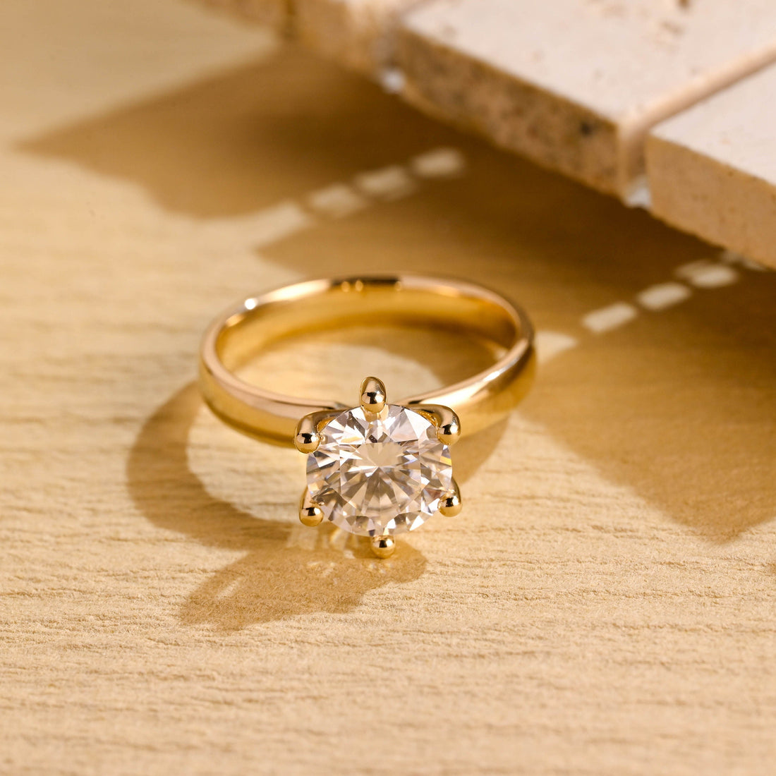 Round moissanite solitaire engagement ring held by six ball tipped claws on a broad polished tapered yellow gold band