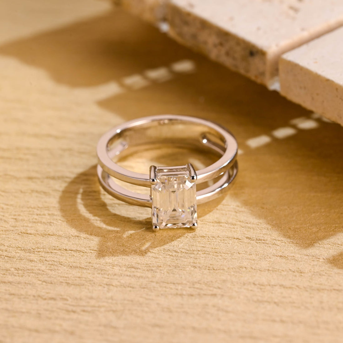 Emerald cut moissanite solitaire engagement ring in four claws set between two parallel polished white gold bands