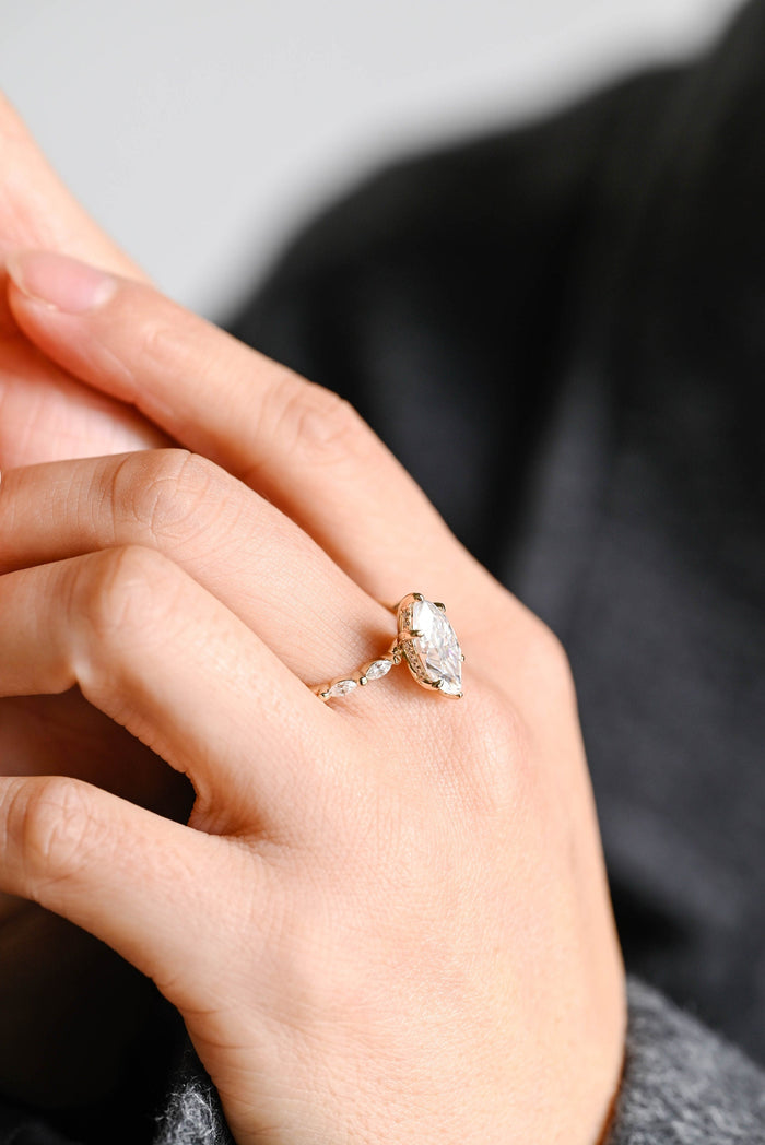 Six claw marquise cut moissanite engagement ring with small marquise stones set along the shoulders of a slim yellow gold band, view 2
