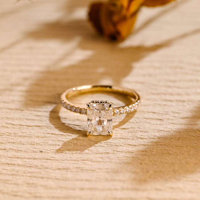 Radiant cut moissanite hidden halo engagement ring in four claws with a slim shared prong pave set yellow gold band