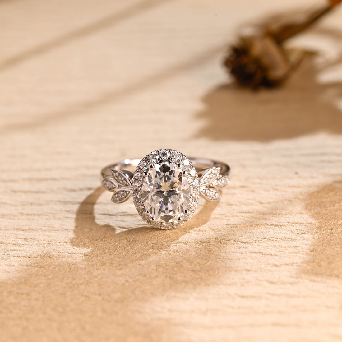 Oval moissanite halo engagement ring with a pave halo and pave set leaves on each shoulder of a white gold band