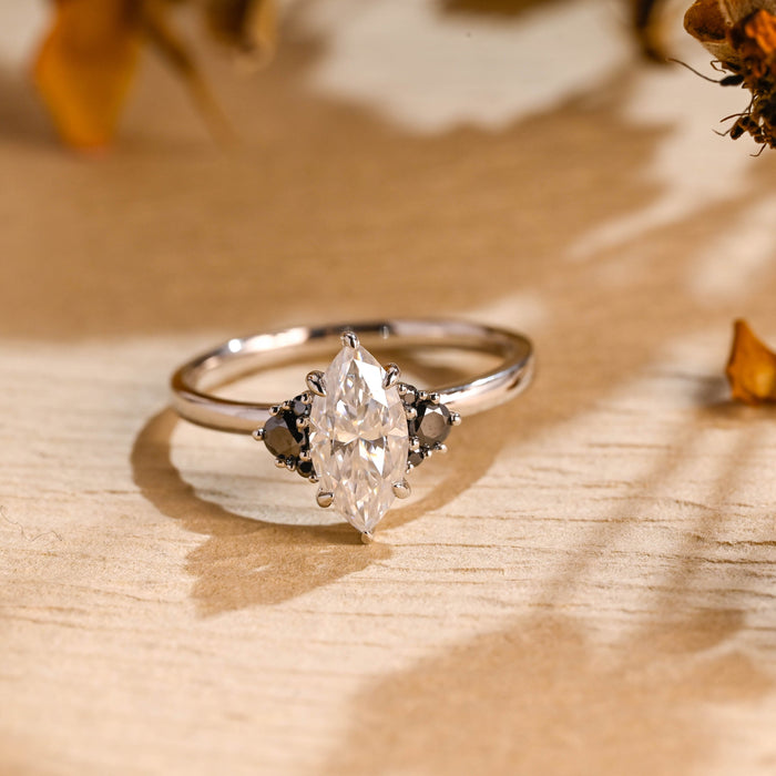 Colourless marquise cut moissanite engagement ring with clusters of black round stones on each side on a slim white gold band