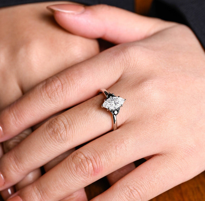 Colourless marquise cut moissanite engagement ring with clusters of black round stones on each side on a slim white gold band, view 2