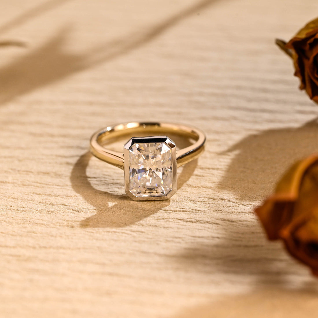Radiant cut moissanite bezel set solitaire engagement ring with a white gold bezel on a tapered yellow gold cathedral band