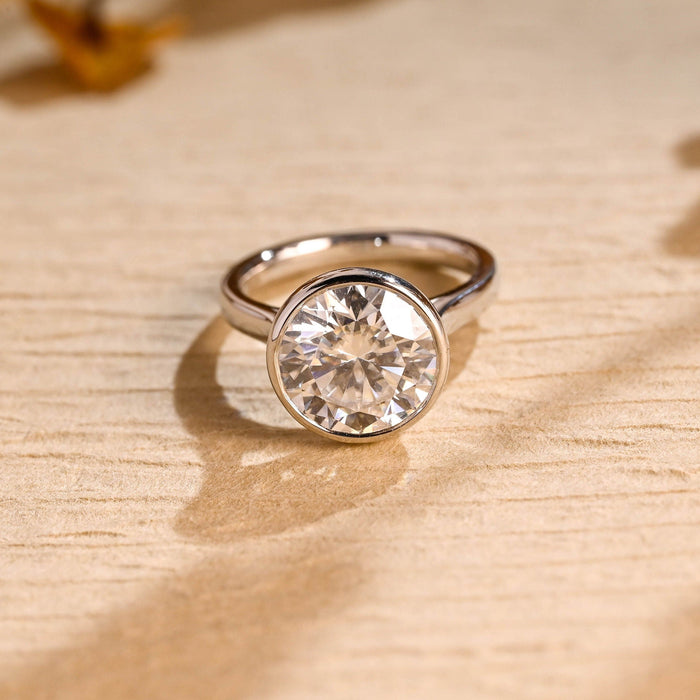 Round moissanite plain bezel solitaire engagement ring with a smooth wide bezel and a plain polished white gold band that tapers up to the stone