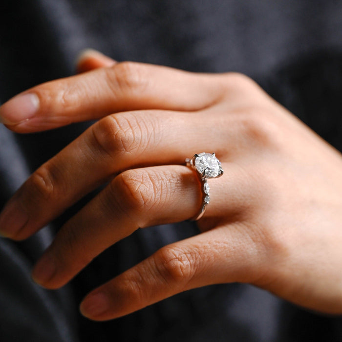 Round moissanite solitaire engagement ring in four claws with a marquise and a small round stone at each shoulder of a slim white gold band, view 2
