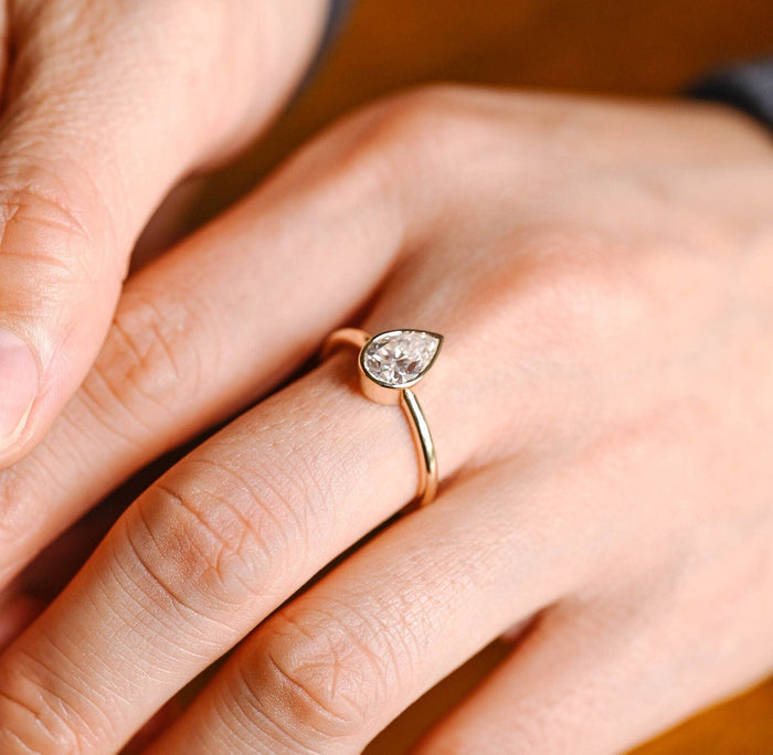 Pear cut moissanite bezel set solitaire engagement ring on a thin polished round yellow gold band, view 2