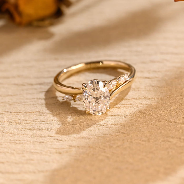 Oval moissanite bypass engagement ring with four claws and two marquise stones on each side of a sweeping yellow gold band