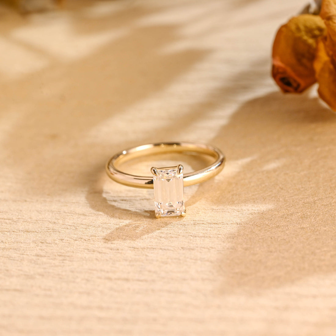 Elongated emerald cut moissanite solitaire engagement ring in four claws on a plain polished round yellow gold band