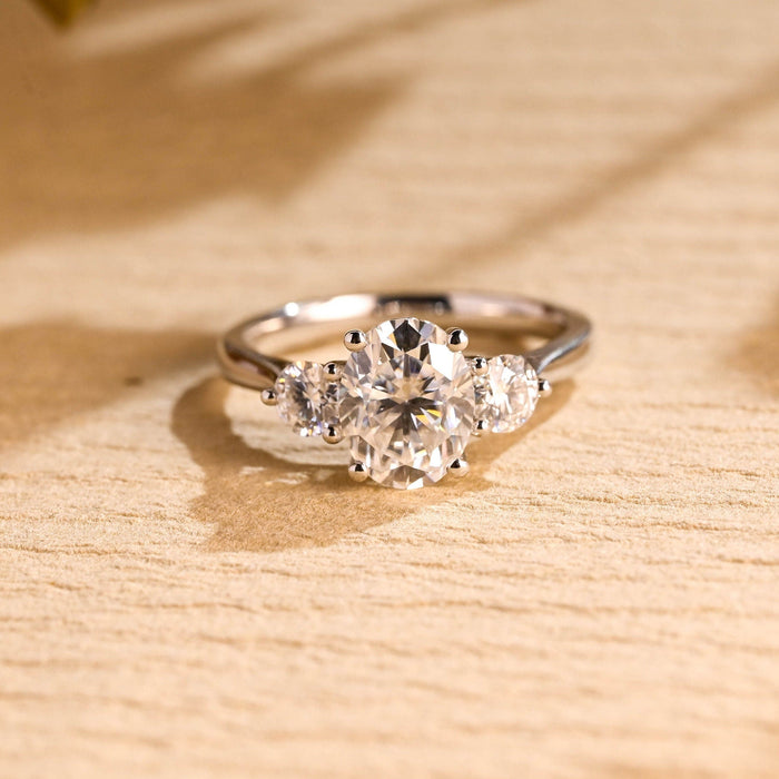 Oval moissanite three stone engagement ring with a round stone on each side on a plain polished tapered white gold band