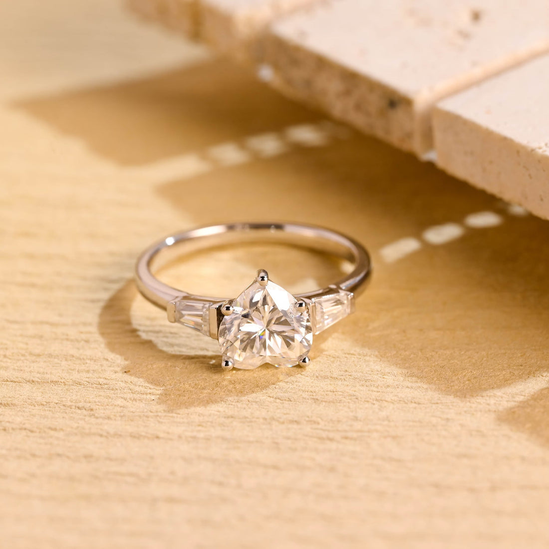 Heart cut moissanite three stone engagement ring with tapered baguette side stones on a white gold band