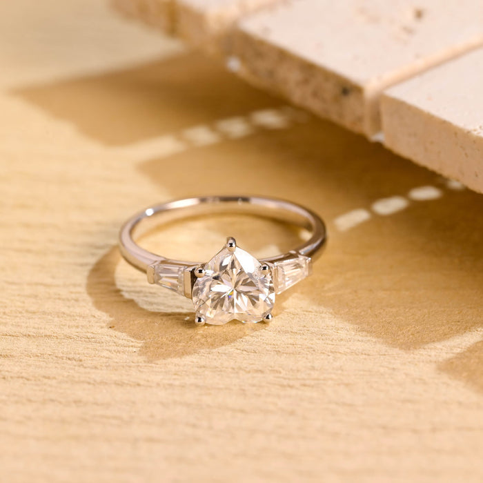 Heart cut moissanite three stone engagement ring with tapered baguette side stones on a white gold band