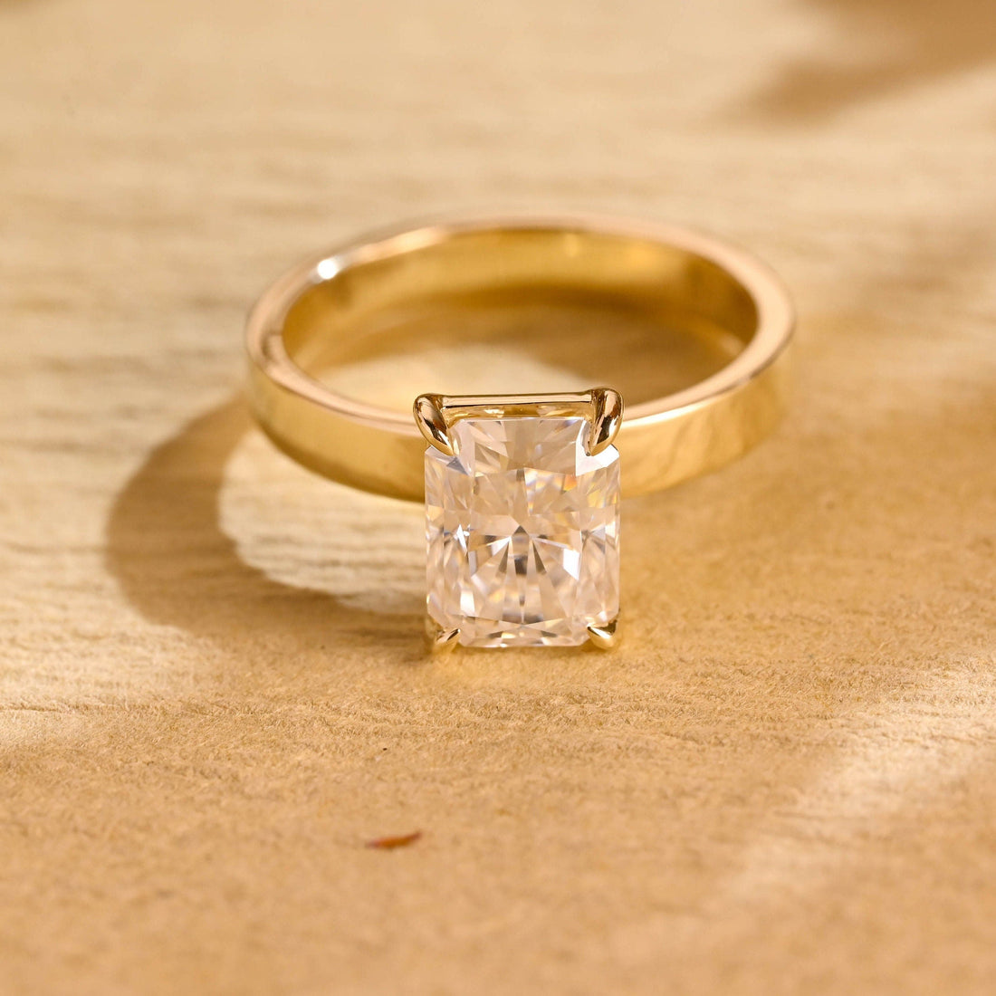 Radiant cut moissanite solitaire engagement ring with four claws on a wide flat polished yellow gold band
